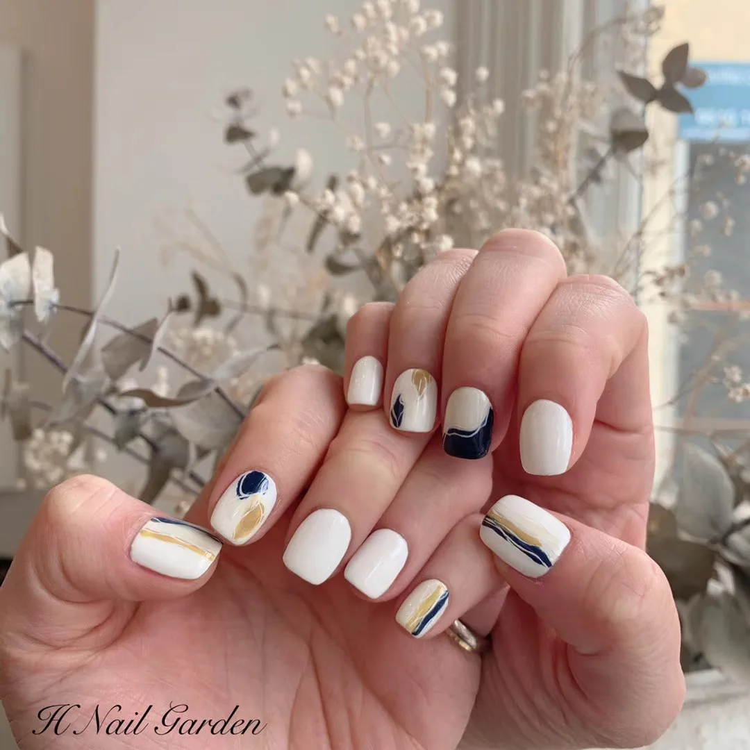 Short white and cream nails with navy and gold marble strokes