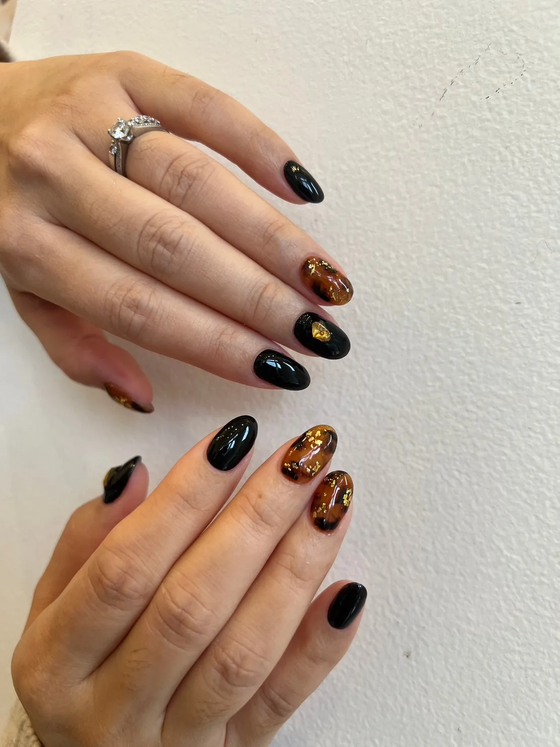 Glossy black and amber tortoiseshell almond nails with gold-foil flecks and a ring