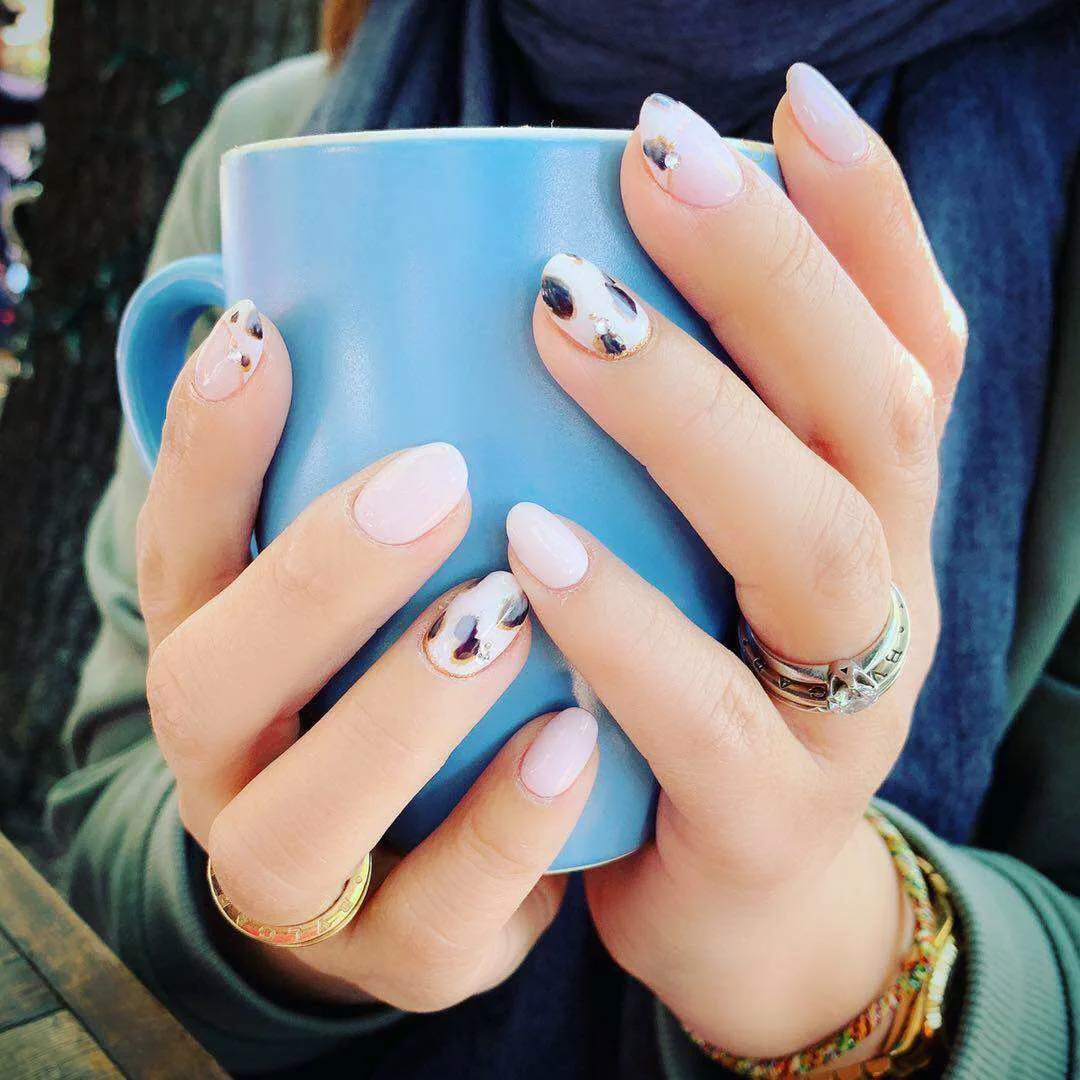 Sheer-pink oval nails with tortoiseshell accents, hands cupping a blue ceramic mug