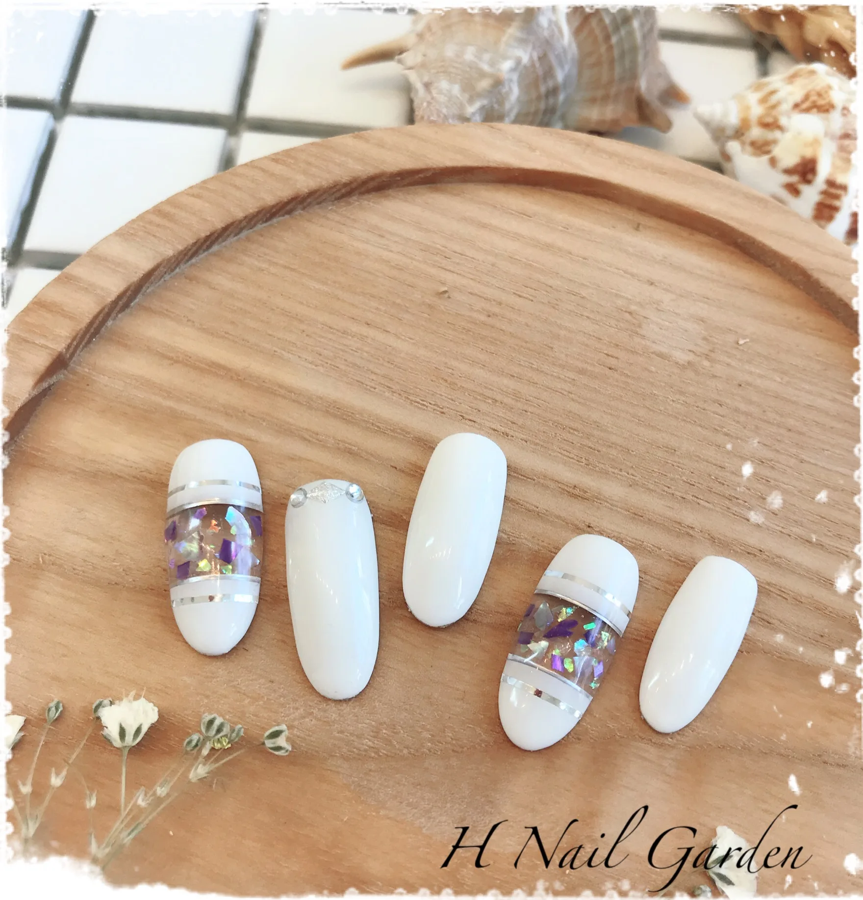 Display nails — white with shell-glitter inlay, arranged on a wood board with seashells and dried gypsophila