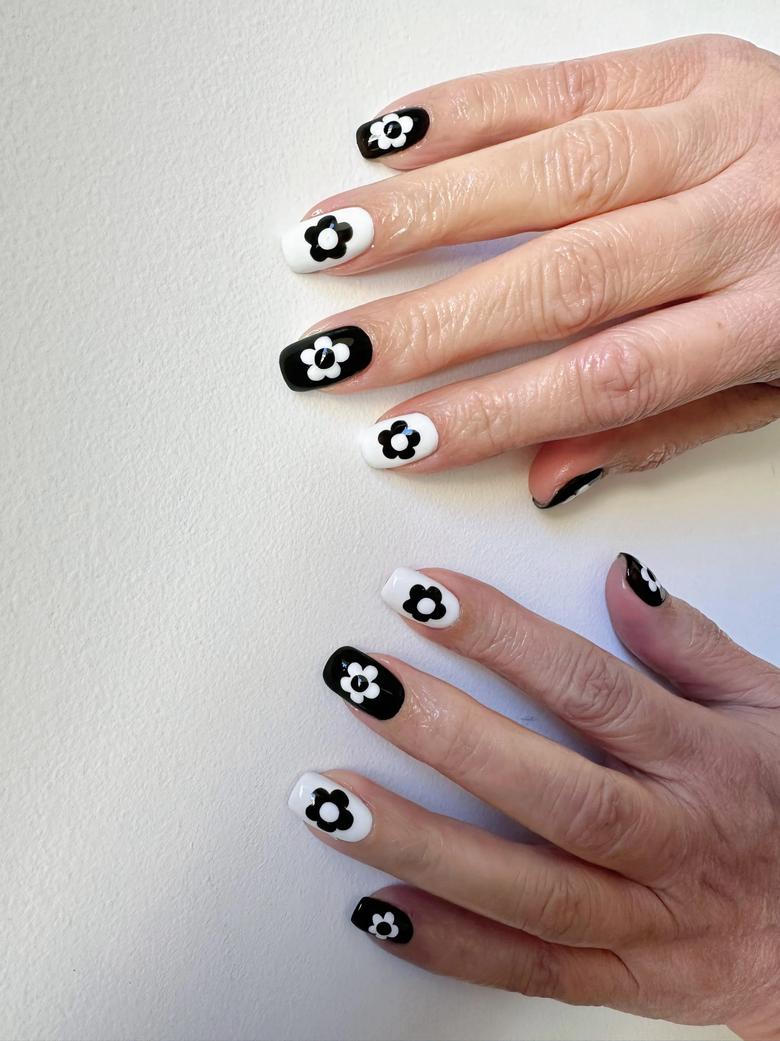 Mod black-and-white daisy and flower nail art on two hands against a pale ground