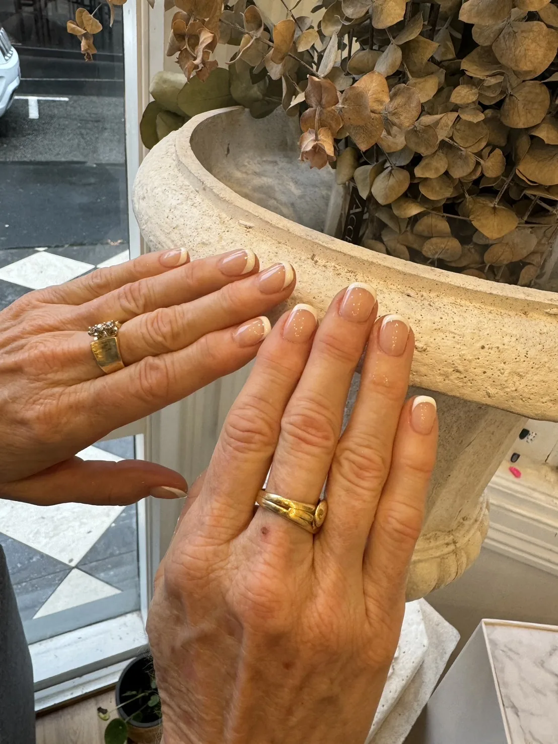 Lilac shimmer nails with silver star accents, hands resting on a stone planter at the salon's arched window