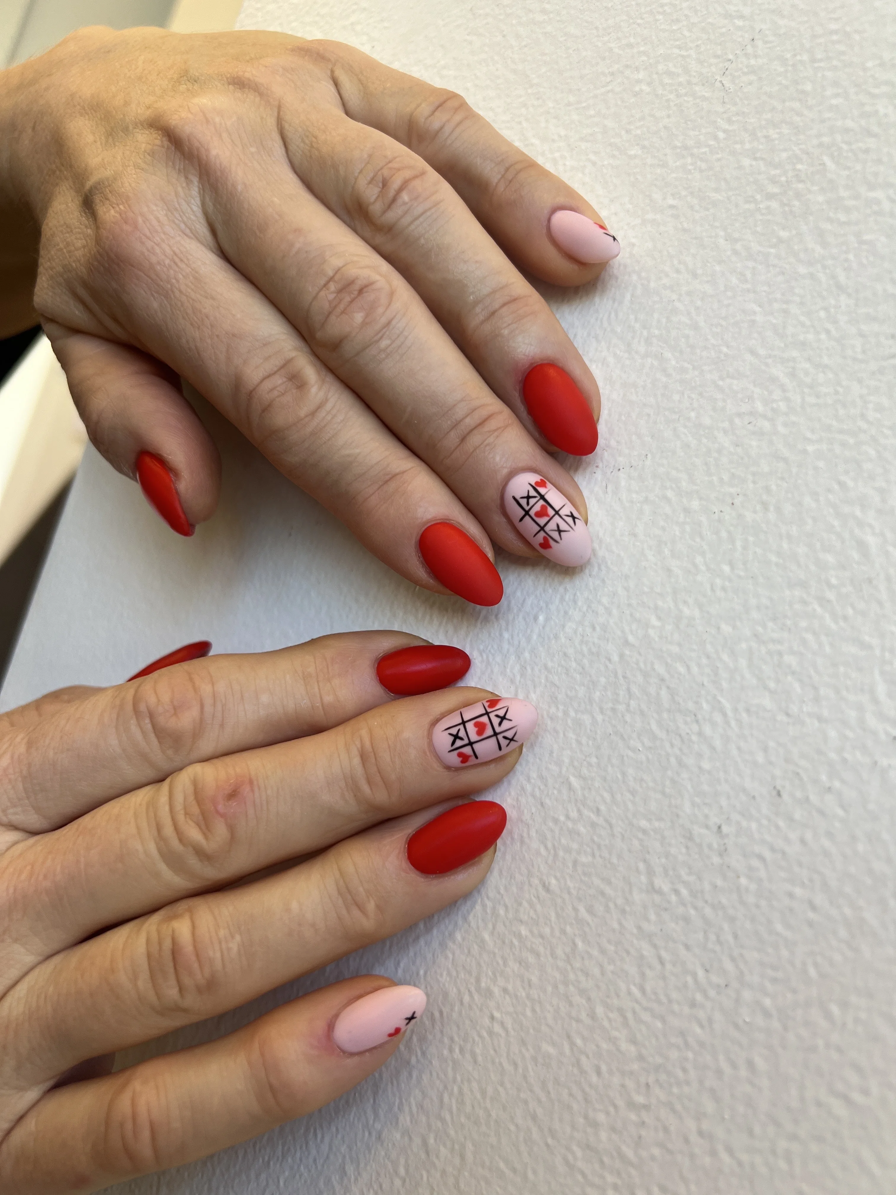 Matte-red nails with a tic-tac-toe-and-hearts accent nail, two hands