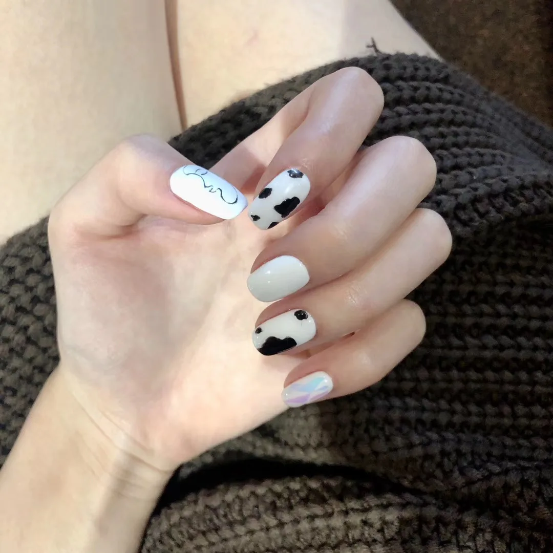 Mixed monochrome set — cow-print, swirl line-work and an iridescent nail, arm in a knit sweater