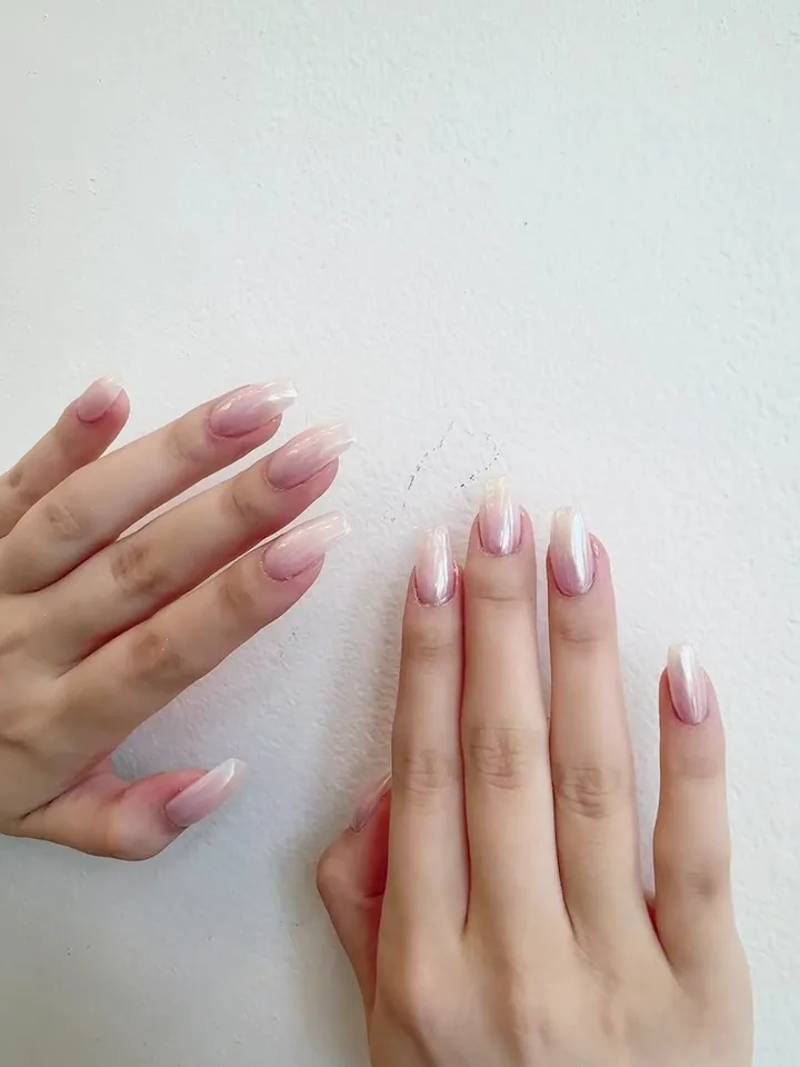 Pearl-chrome pink ombré almond nails, two hands against a wall