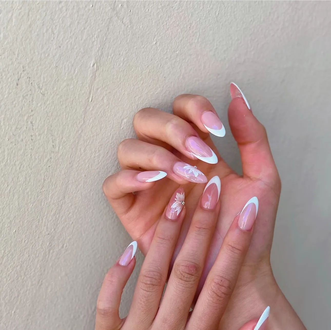 Almond nails — iridescent nude with crisp white French tips and a hand-painted floral accent