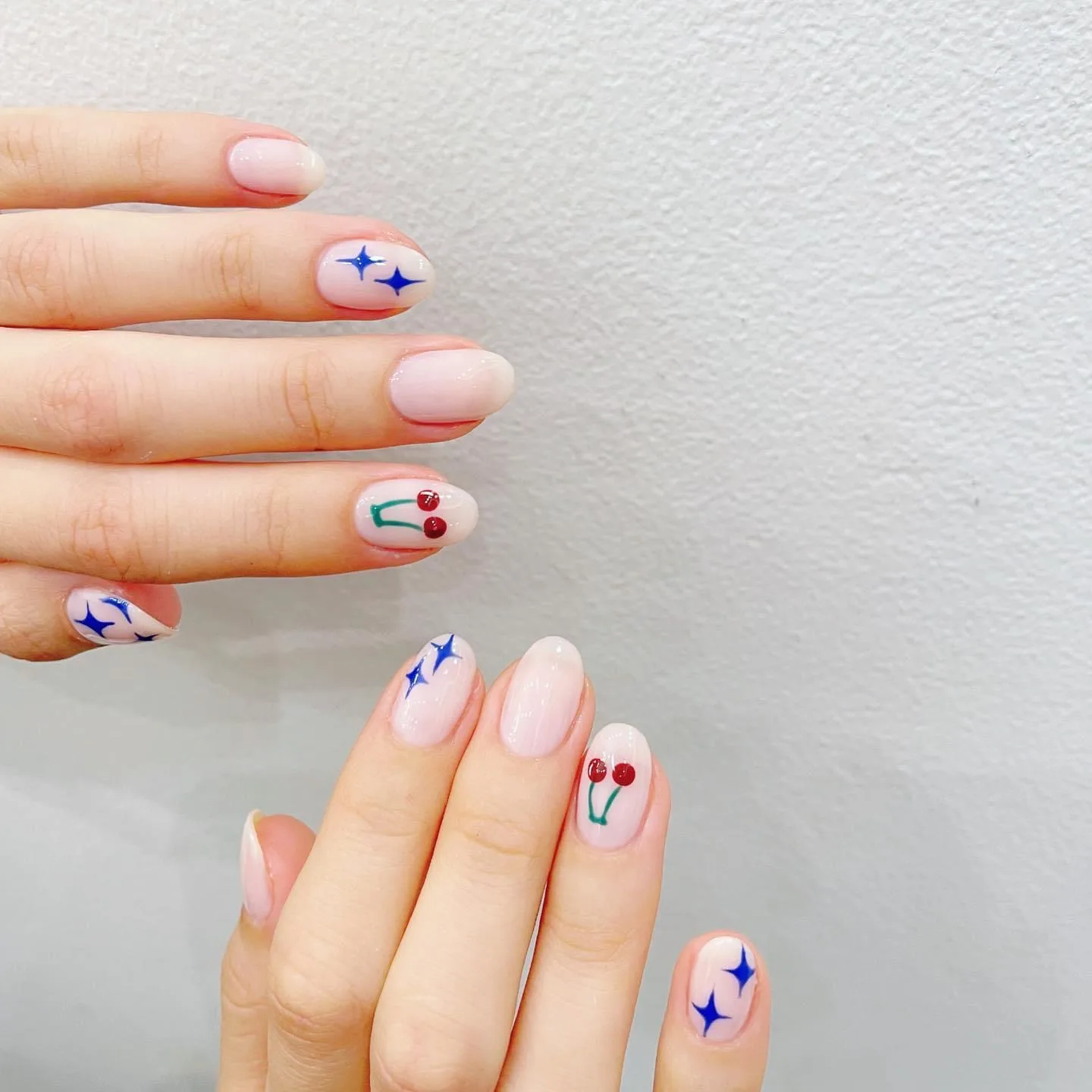 Sheer nude nails with navy sparkle bursts and hand-painted cherries